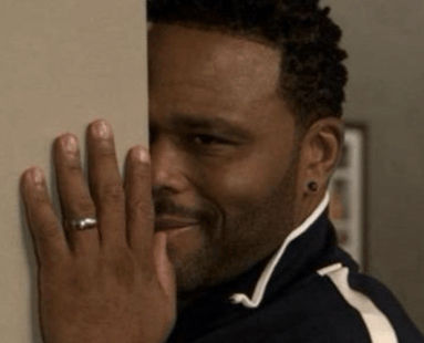Man peeks from behind a wall with a sly smile, hand raised with a ring visible in a dim indoor setting. Client and designer reviewing creative concepts while defining subjective terms such as industrial, colorful, and tasteful through visual references