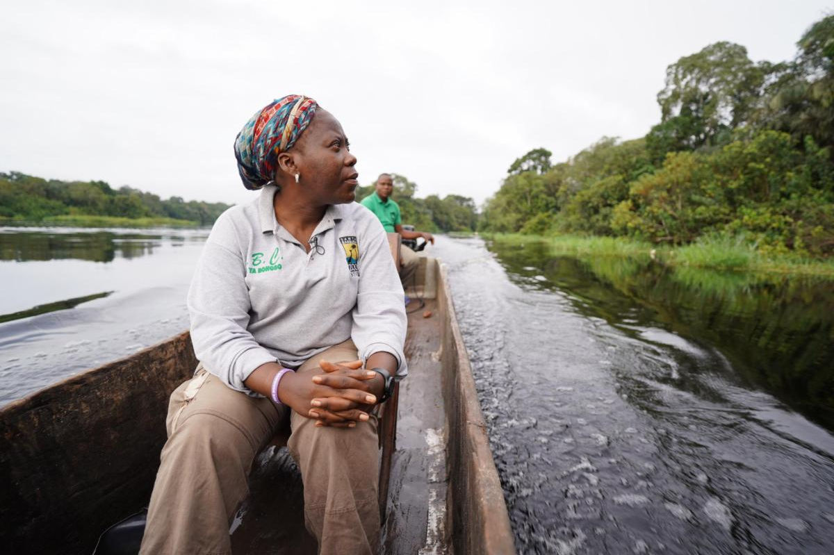 Woman sitting in canoe on a dark river in DR Congo with shoreline in background