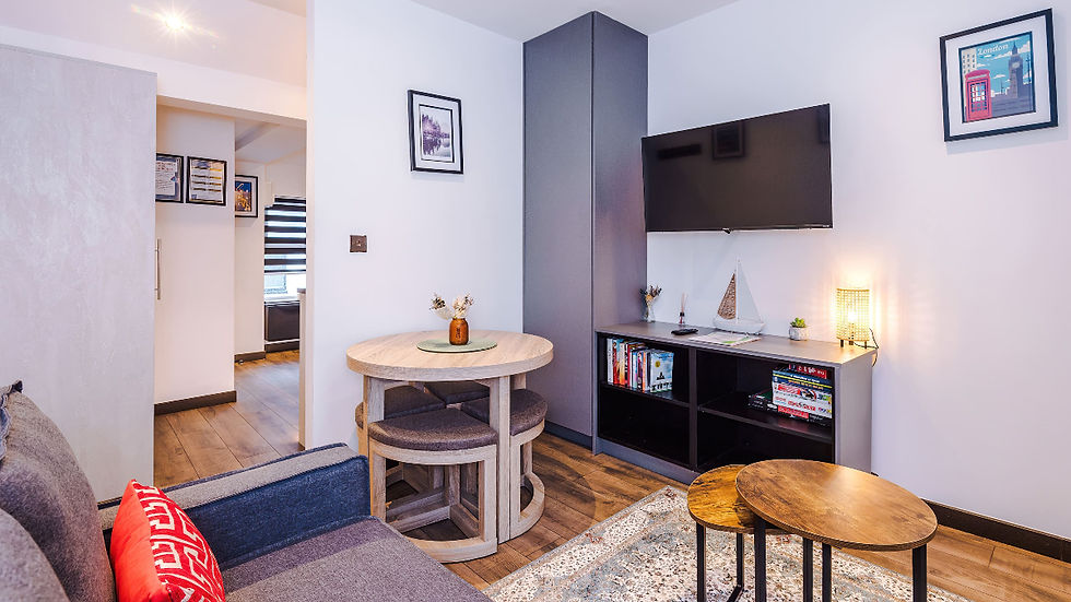 rainy day Llandudno Modern living room with gray sofa, round table, wall TV, lit lamp, bookshelves, and London print art in a cozy setting by Llandudno Great Escapes