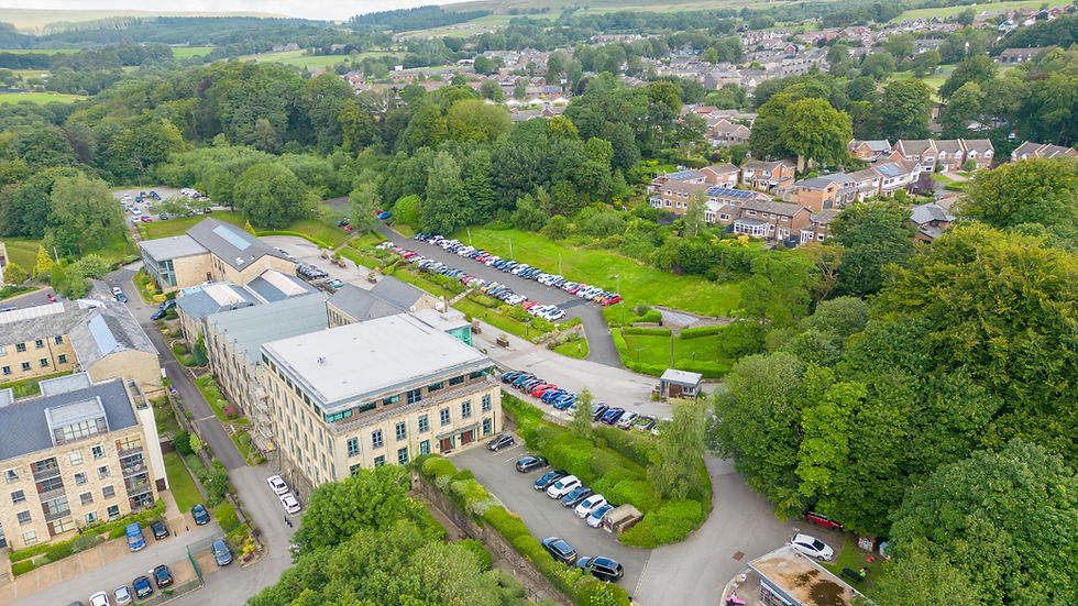 serviced accommodation Bolton Aerial view of a leafy hillside campus with stone buildings, packed parking lots, and a town beyond under green hills by DBR Lettings.