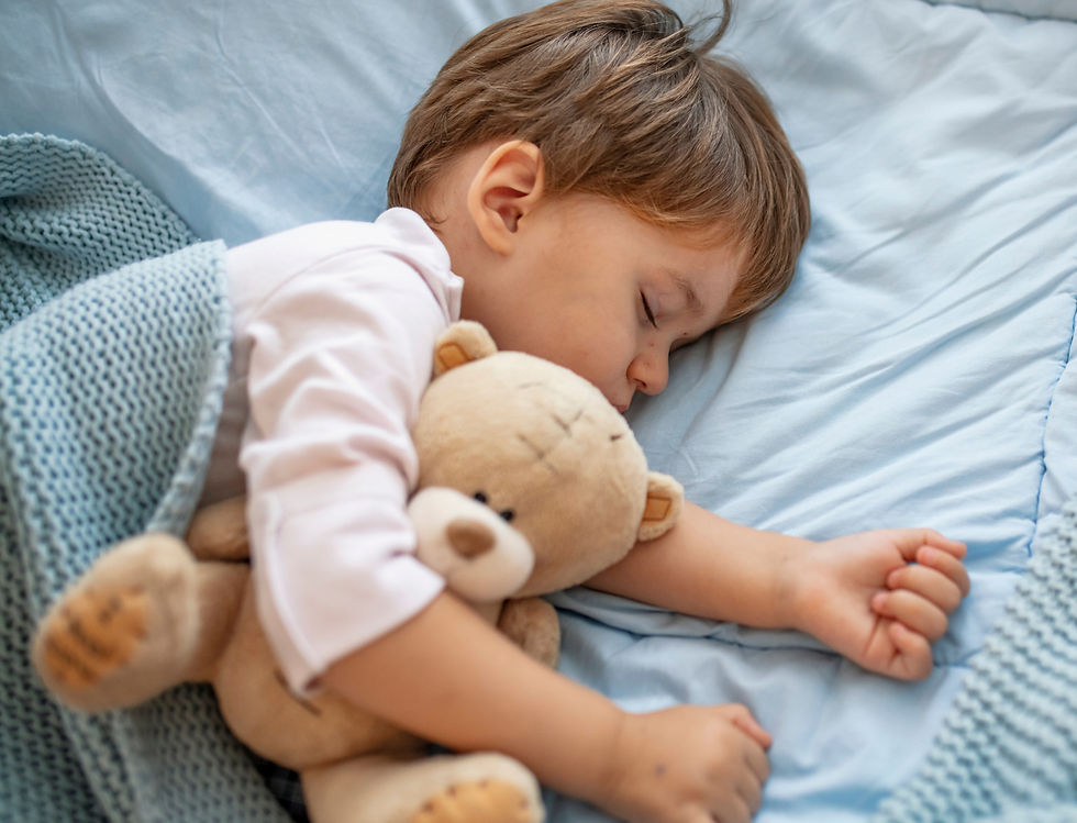 little boy lying down sleeping peacefully in his bed while snuggling his teddy bear.
