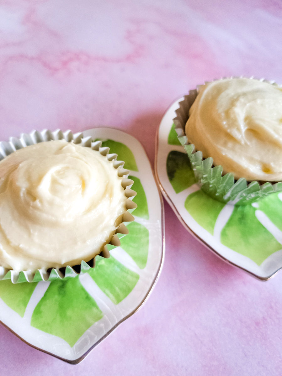 A pink marble tabletop, two leaf shape green plates with pale orange mango cupcakes