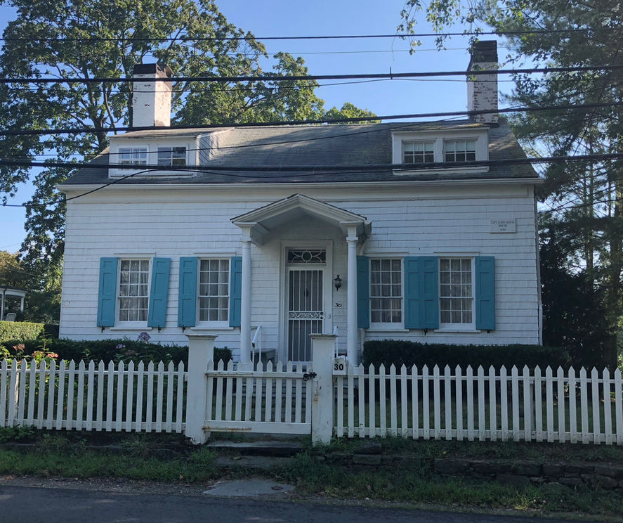 White clapboard house with blue shutters, white picket fence in protected historic district