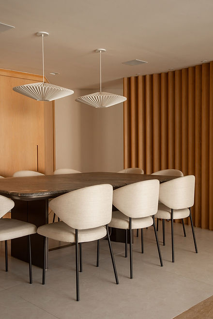 Sala de jantar moderna com mesa de pedra, cadeiras estofadas e pendentes decorativos em ambiente de tons neutros e painel de madeira.