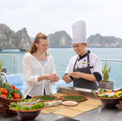 Chef and guest on the sundeck of Luna Halong Cruise with a fresh fruit spread and Halong Bay in the background