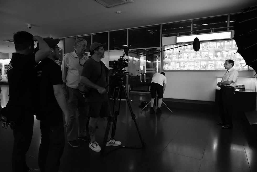 Film crew member with "2BIG Production" shirt operates a camera on a bustling set with bright, colorful lighting and industrial decor.