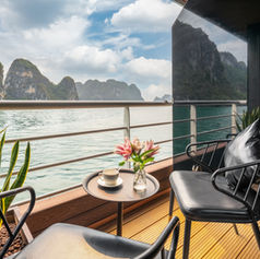 Private balcony cabin on Luna Halong Cruise with rattan chair, side table and unobstructed limestone karst views

