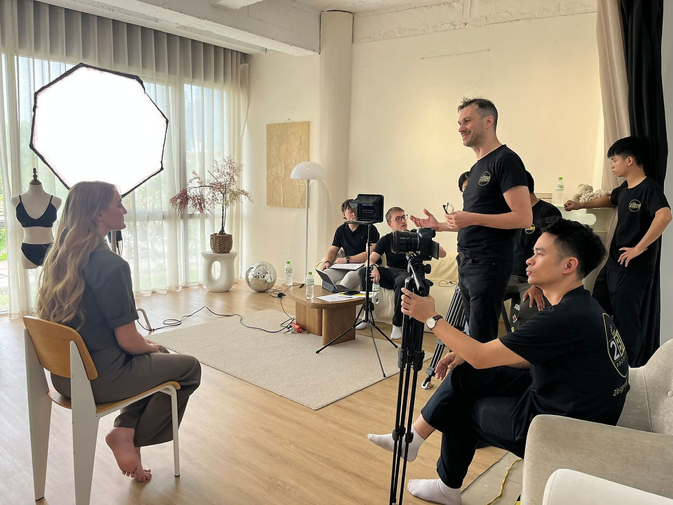 Video Director briefs seated woman in a bright studio while crew films with lights, camera, and tripod; casual, focused mood.