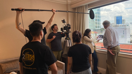 2BIG Production filming crew and audio technician with boom mic filming inside a hotel by a window overlooking Ho Chi Minh City