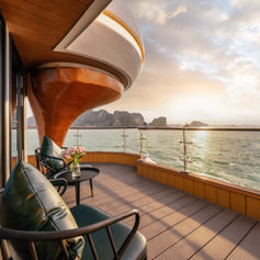 Curved private balcony on Luna Halong Cruise with lounge seating and panoramic sunset view over Halong Bay