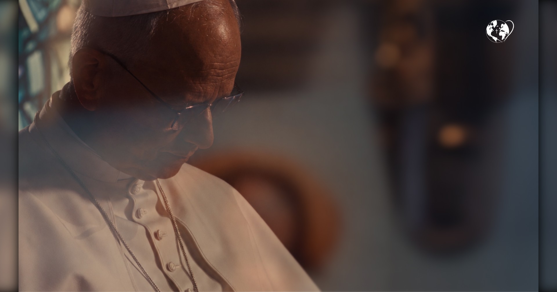 Pope Leo XIV, seen from the side in a white zucchetto, glasses and white cassock, his head bowed in prayer. Behind him the room is in soft, warm shadow, and the globe emblem of the Pope's Worldwide Prayer Network sits in the top right corner.