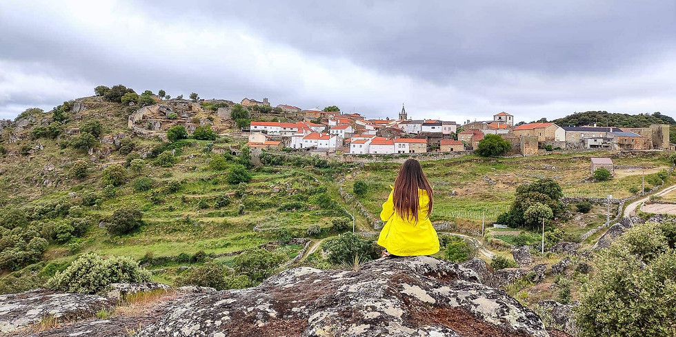 Hiker woman sitting on rock looks at Castelo Mendo historic village