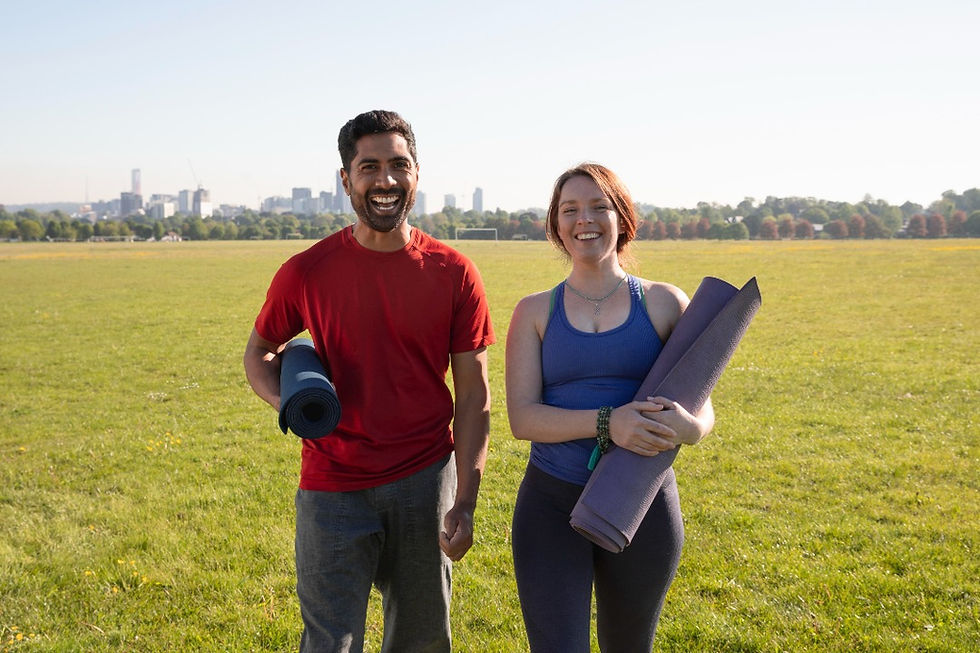 Man and woman smiling as they hold yoga mat in a park on a sunny day