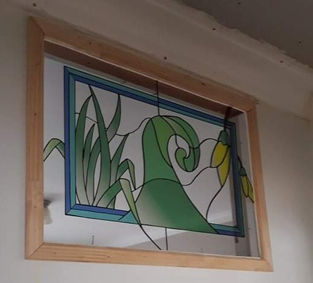 Stained glass window with green plant design and light wooden frame.