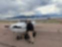 Student pilot standing with flight gear in front of a Cessna trainer aircraft with the Rocky Mountains in the background
