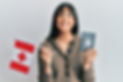 Young hispanic woman holding canada flag and passport smiling with a happy and cool smile