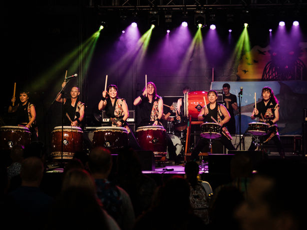 JGB Shibuki performing with 7 drummers on a stage lit with green and purple lights.