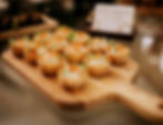 Private Chef Marcel - Dinner in Stamford. Mini tarts with cream and greens on a wooden board, set in a dimly lit room with blurred background details.