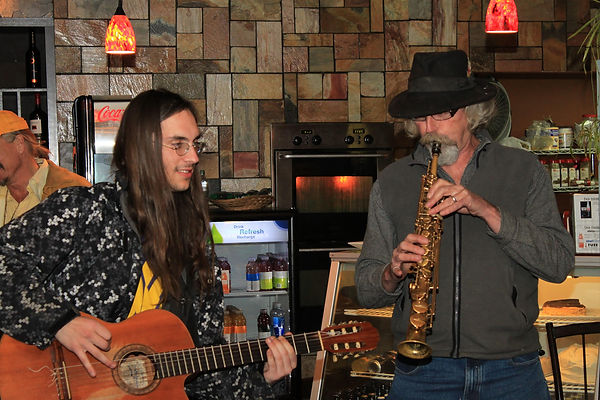 Ross Campbell playing a saxophone alongside a guitarist in a cozy café setting.