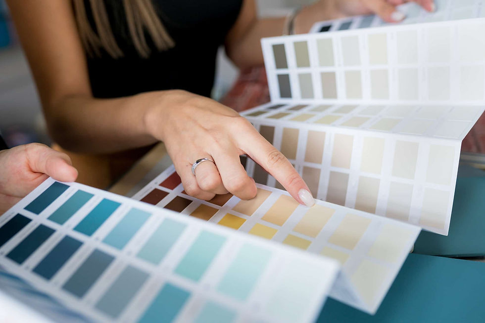 Hands examining a color palette, pointing at beige swatches. Background shows blue-green shades. Focused, decision-making mood. Color consultation.