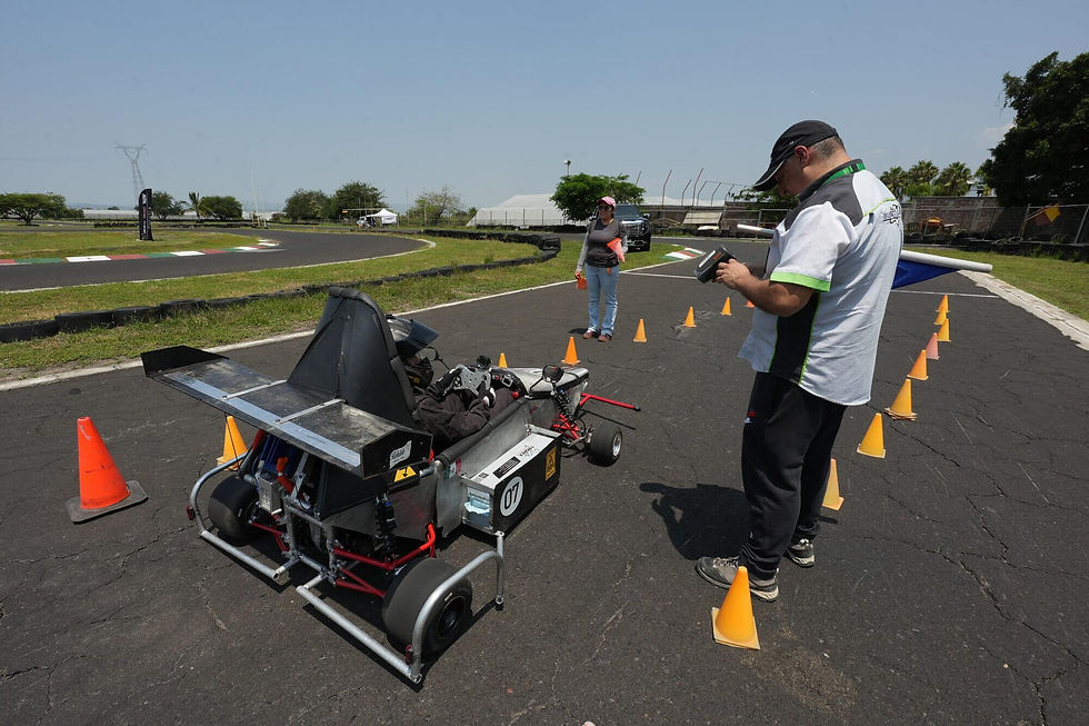 Kart de carreras en pista de pruebas; un hombre revisa un dispositivo y una mujer espera entre conos bajo cielo despejado.