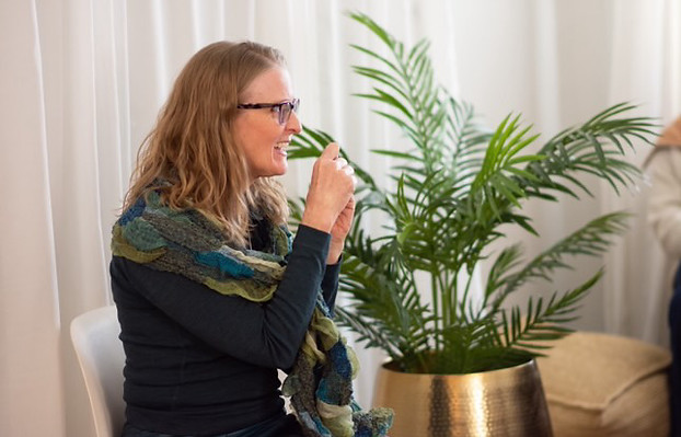 Lea Appleton sitting and speaking to a group of people. Plan and curtain are in the background.