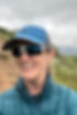 Coach Lea Appleton wearing white sunglasses, a blue cap, and a green puffy jacket smiling.