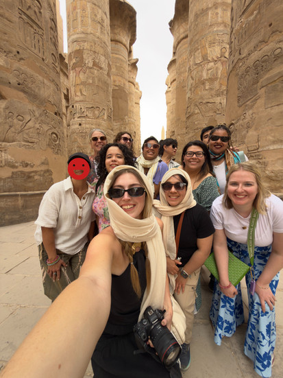 a group of people taking a selfie between tall pillars with egyptian artwork 