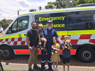 Taycee-Lea Jones in her paramedic uniform posing in front of an ambulance with her family