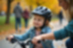 Child with helmet riding a bike in a park, guided by an adult. Autumn trees in the background, child smiling, wearing a denim jacket.