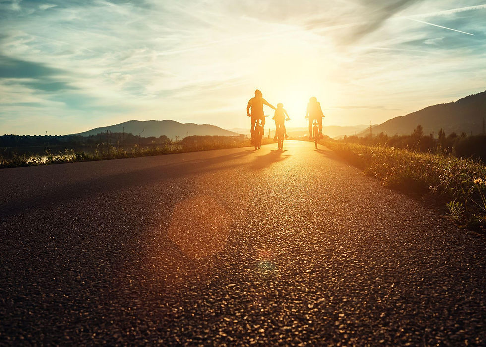 Silhouetted group cycling on a sunlit road at sunset, surrounded by mountains. Warm orange glow creates a serene, joyful atmosphere.