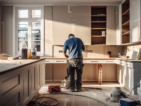 Worker in a blue shirt assembling a kitchen in a sunlit room. Cabinets and tools scattered amid warm light, creating a focused atmosphere.