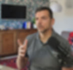 Coach Stefano Calvetti is intent on an online conversation. He is seated and a microphone is visible- His right hand is moving with his index finger extended upward.