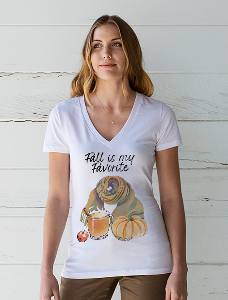a woman wearing a t-shirt featuring "Fall is my favorite", a scarf, hot apple cider, a pumpkin and an apple