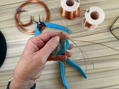 A rural Alberta metalsmith's hands at the bench, wrapping copper wire around a blue fire agate