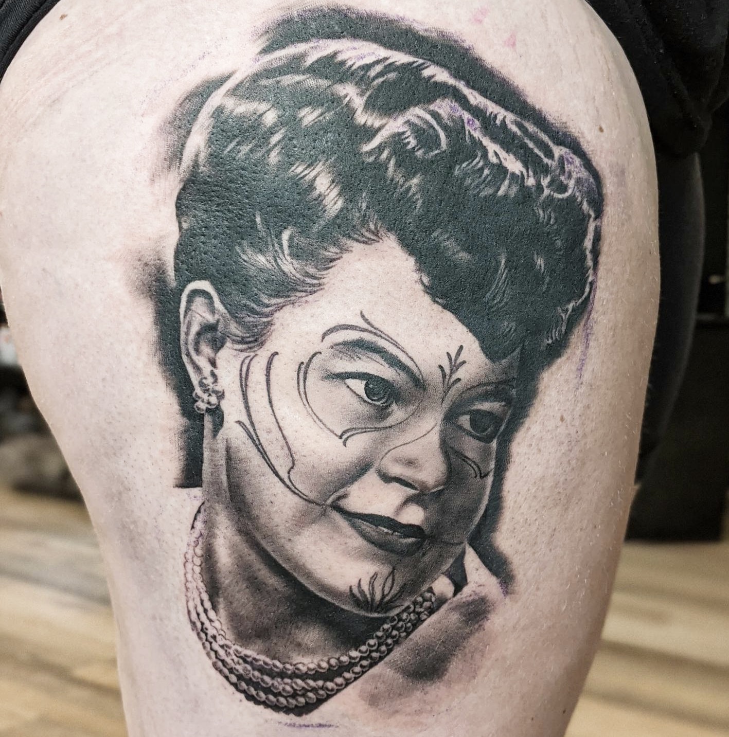 Black and grey realistic portrait tattoo of a woman with an upswept hairstyle and a beaded necklace, on a thigh