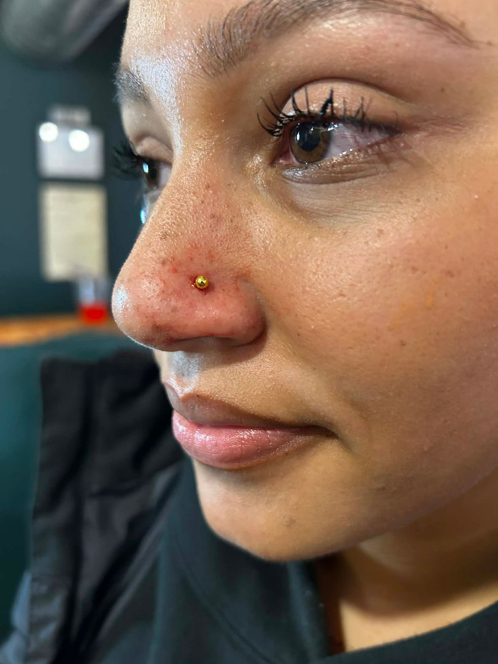 Young woman with nose piercing smiling, freckles visible, close up shot.
