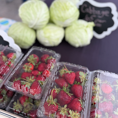 Plastic containers of fresh strawberries and heads of cabbage are displayed at a market produce stand.