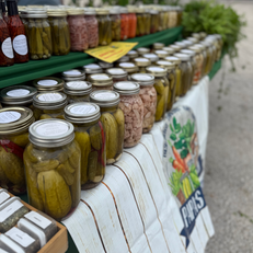 A market stall displays rows of jars filled with pickles and preserves, neatly arranged on a table.