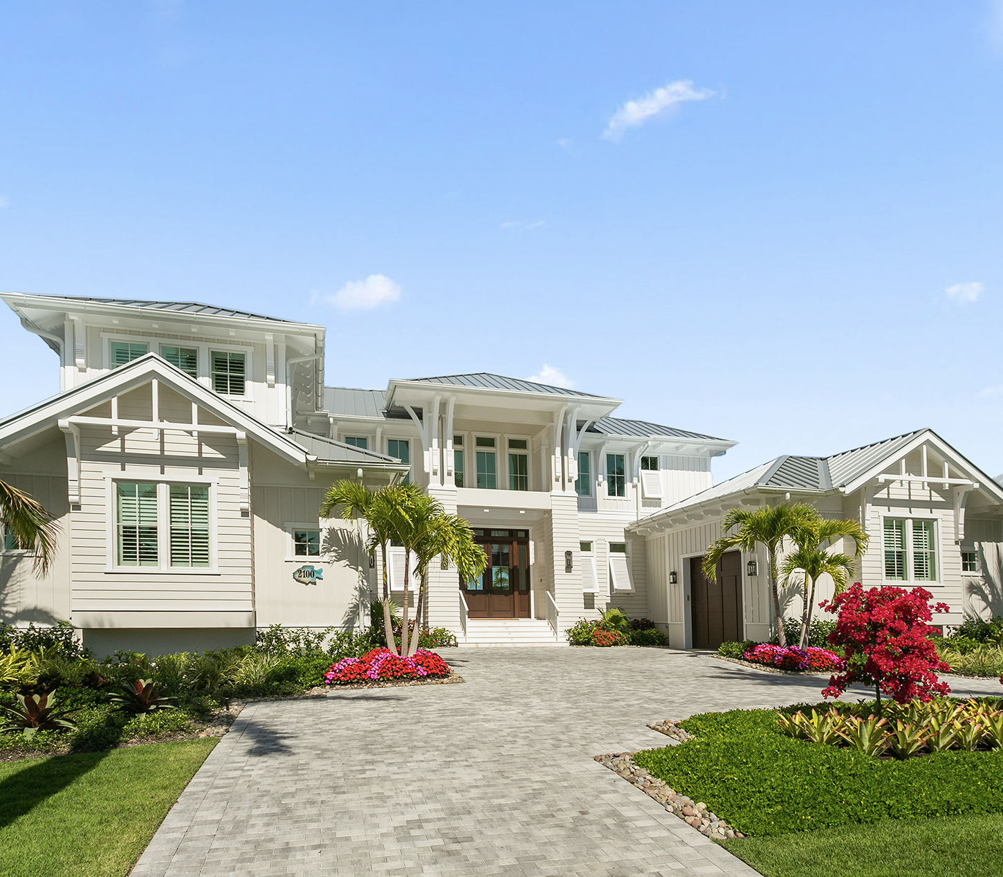 Custom coastal luxury home with white exterior, metal roof, tropical landscaping, and elegant curb appeal.