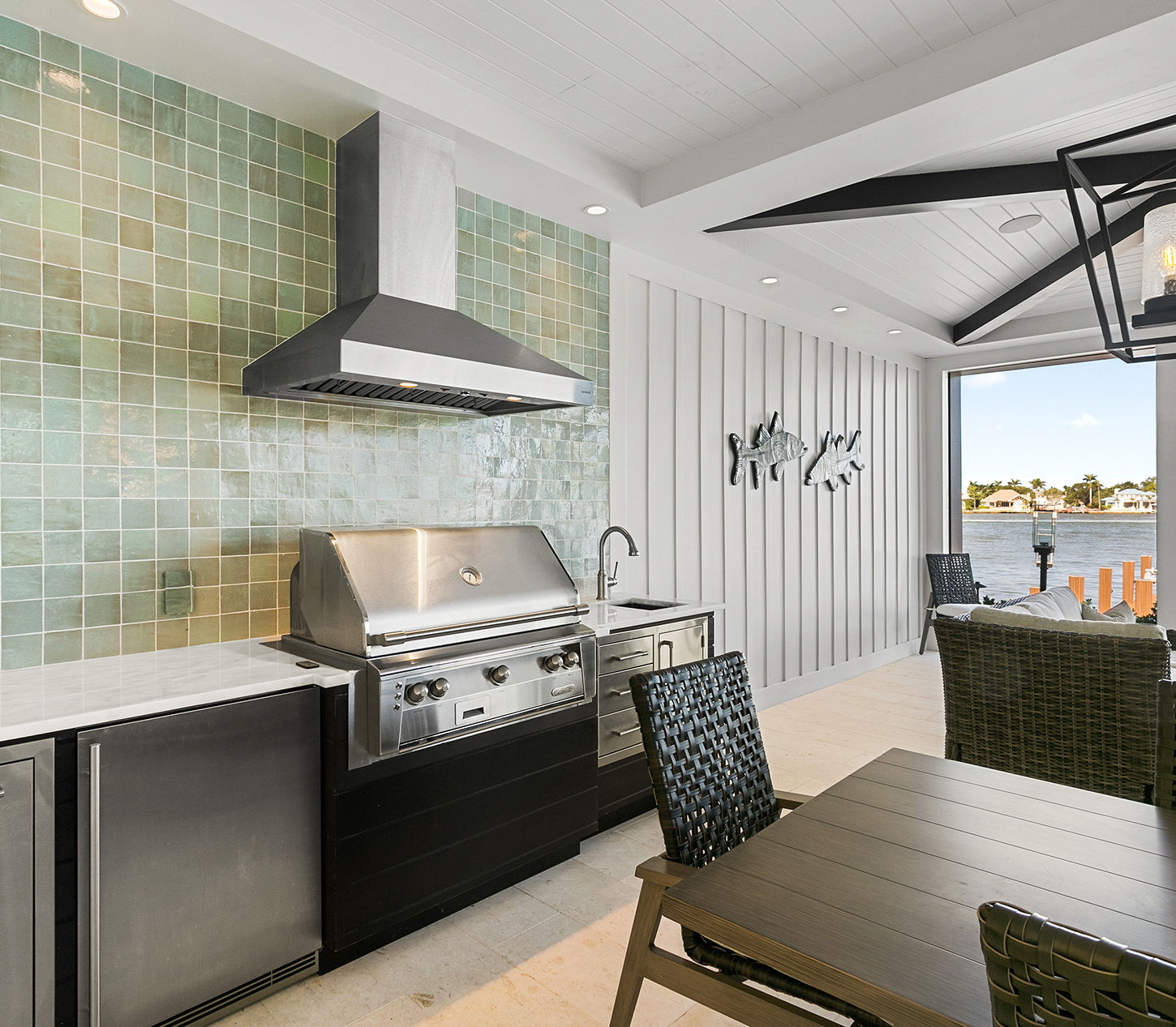 Covered outdoor kitchen with built-in grill, dining area, and seamless indoor-outdoor living overlooking the waterfront.