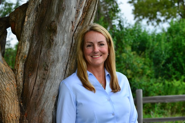 Smiling woman in light blue shirt leaning against a tree.