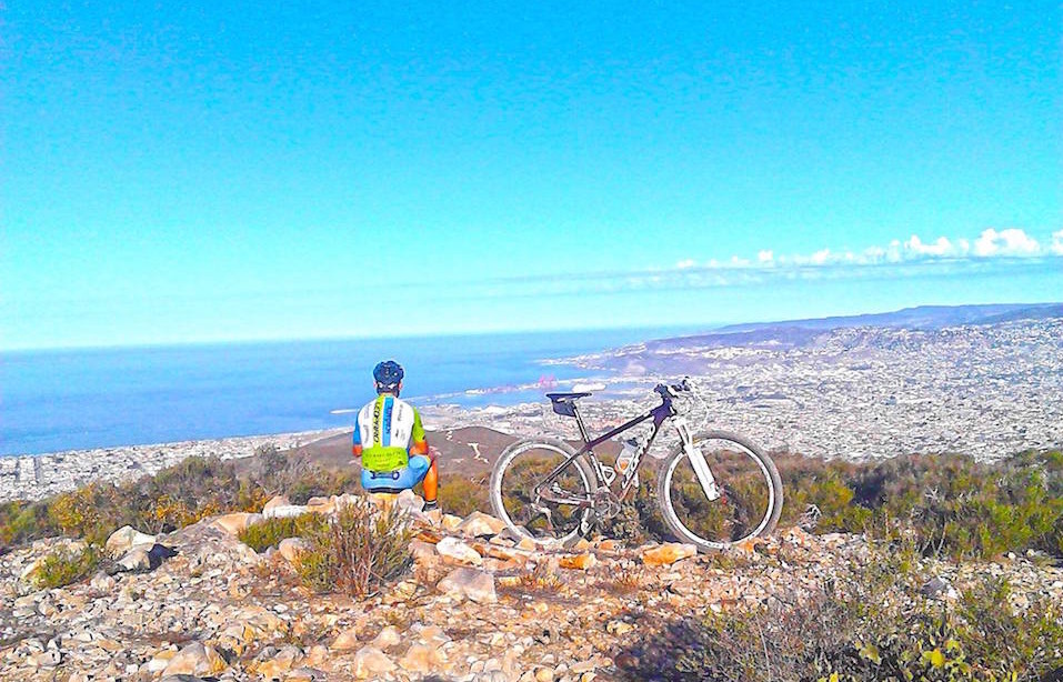 Cyclist resting on a hilltop overlooking a coastal city.
