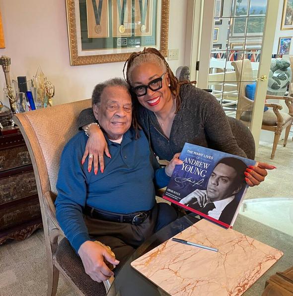 Andrew Young and a woman posing with his book in a home setting.
