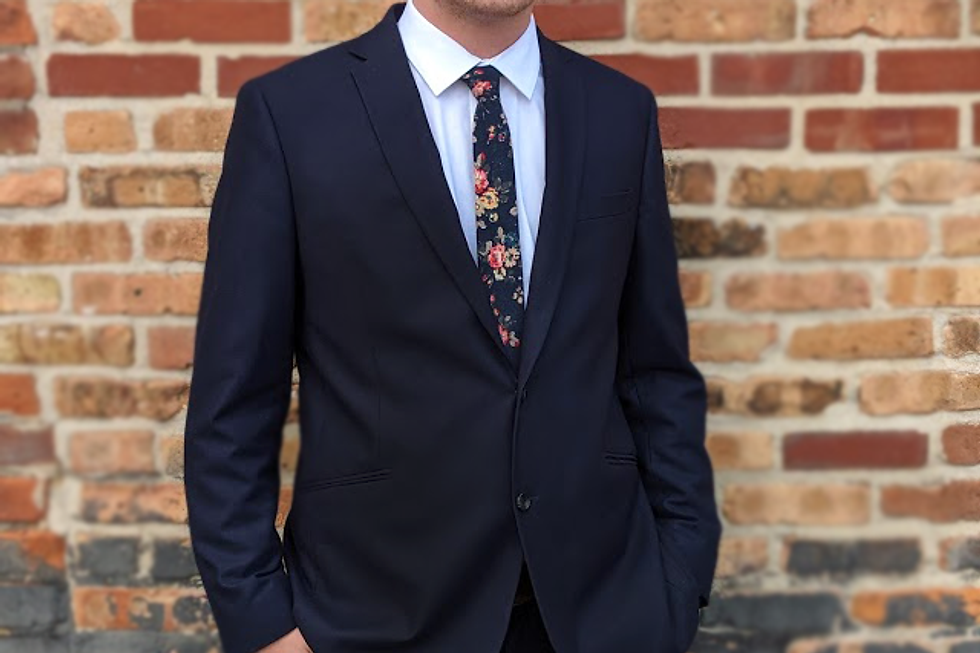 Professional man in a dark suit against a brick wall.