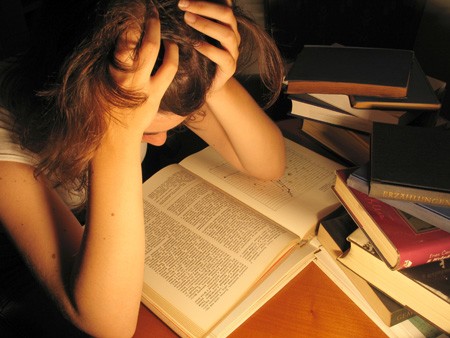 Stressed person holding head over open books while studying