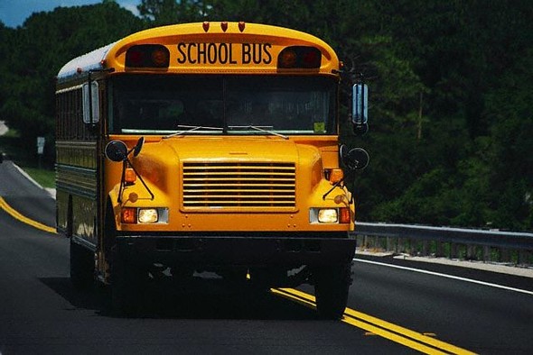Yellow school bus driving on a paved road with trees.