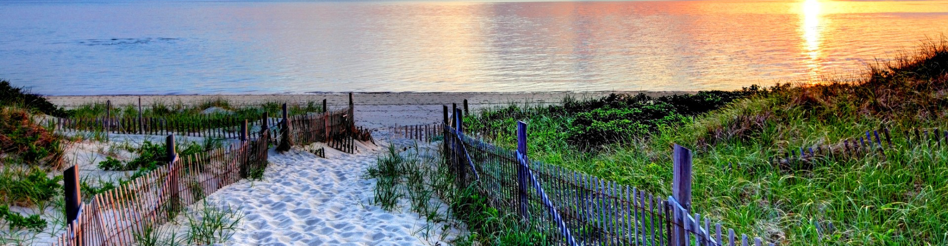 Sand path between fences leading to a beach at sunset