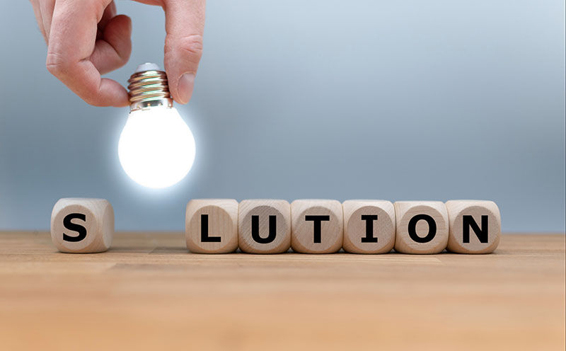 Hand placing glowing bulb over blocks spelling solution