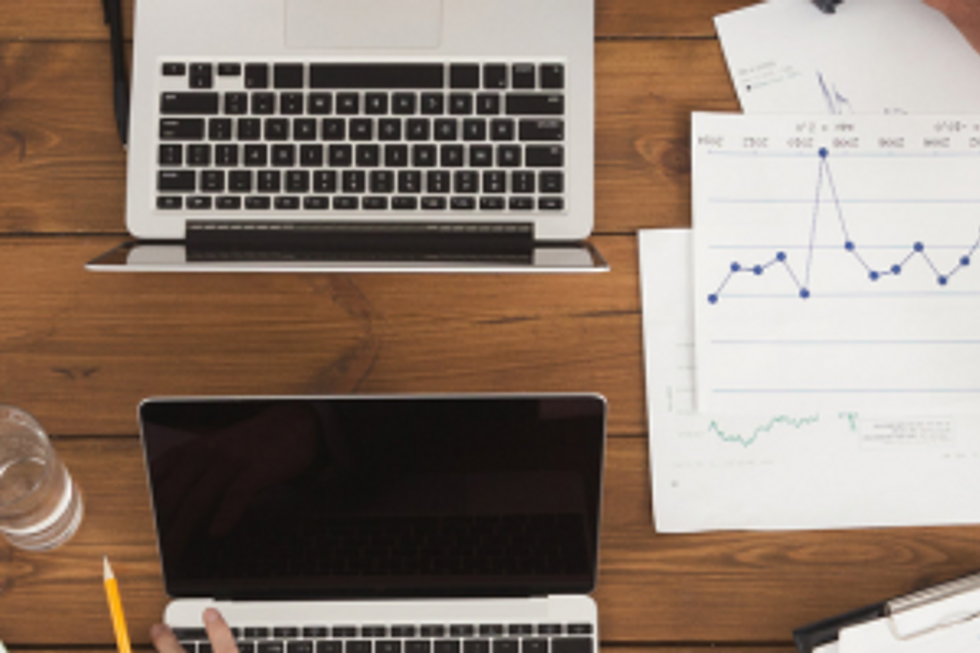 Overhead view of laptops and financial charts on a desk.